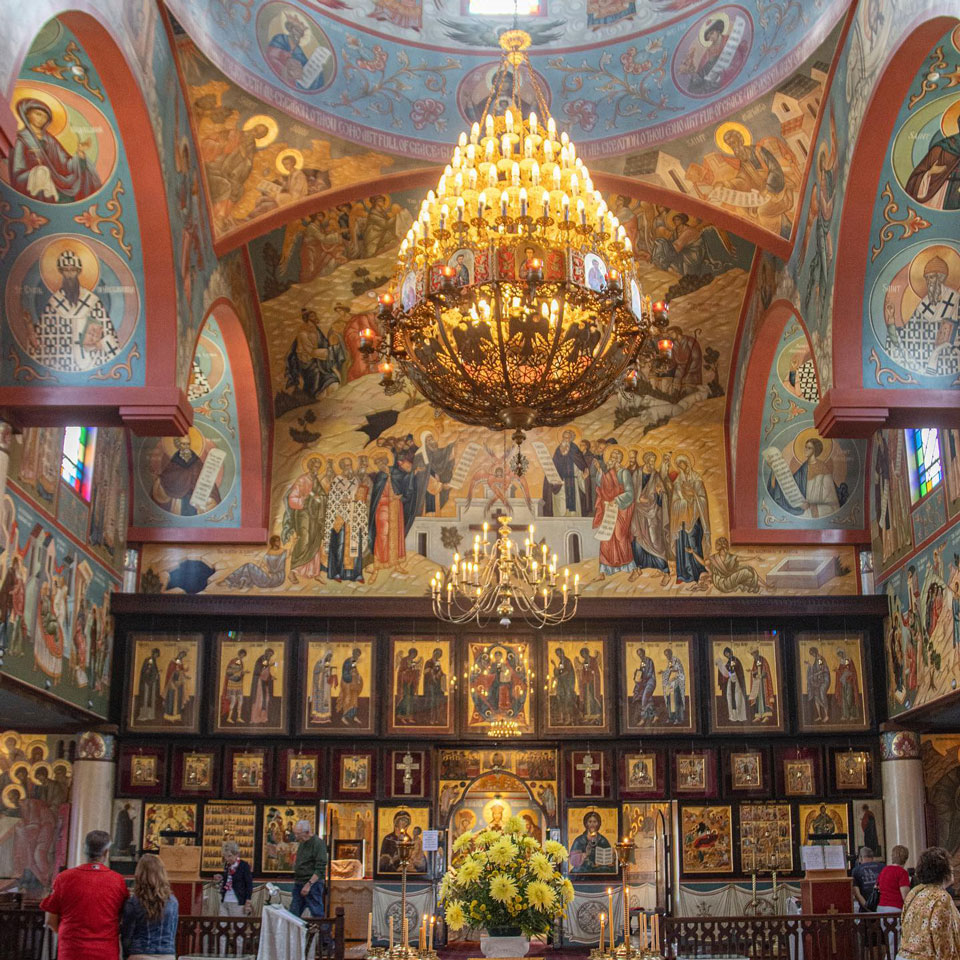 A chandelier hanging from roof inside a church with beautifully painted art work all over