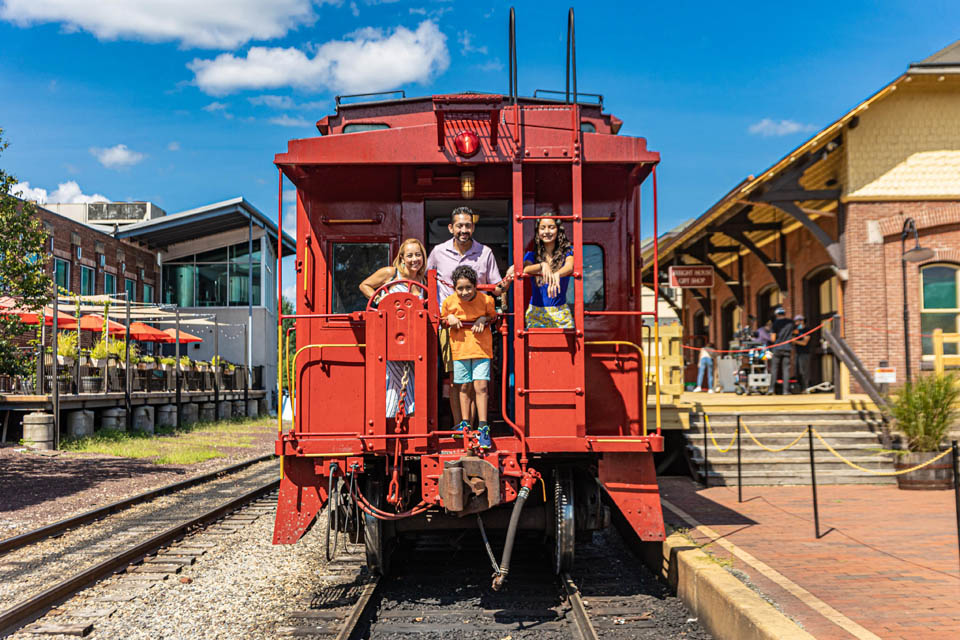 A family posing for a photo standing behind train car box