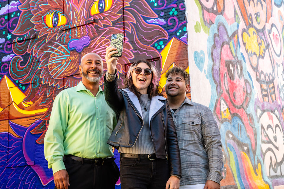 Group of 3 taking a selfie infront of mural