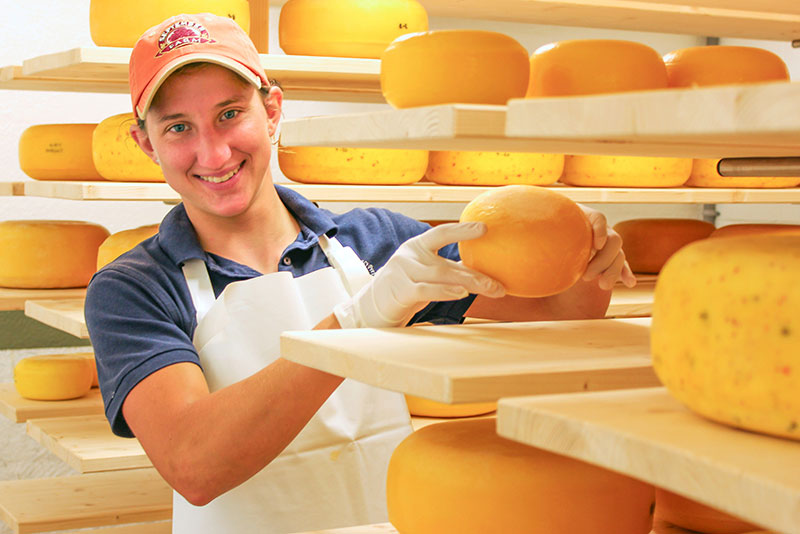 person holding cheese inside cheese storage room