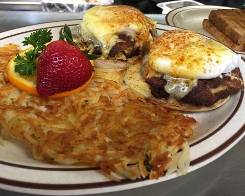 burger with an omlet on top with a side of hash brown topped with a slice of orange and stawberry