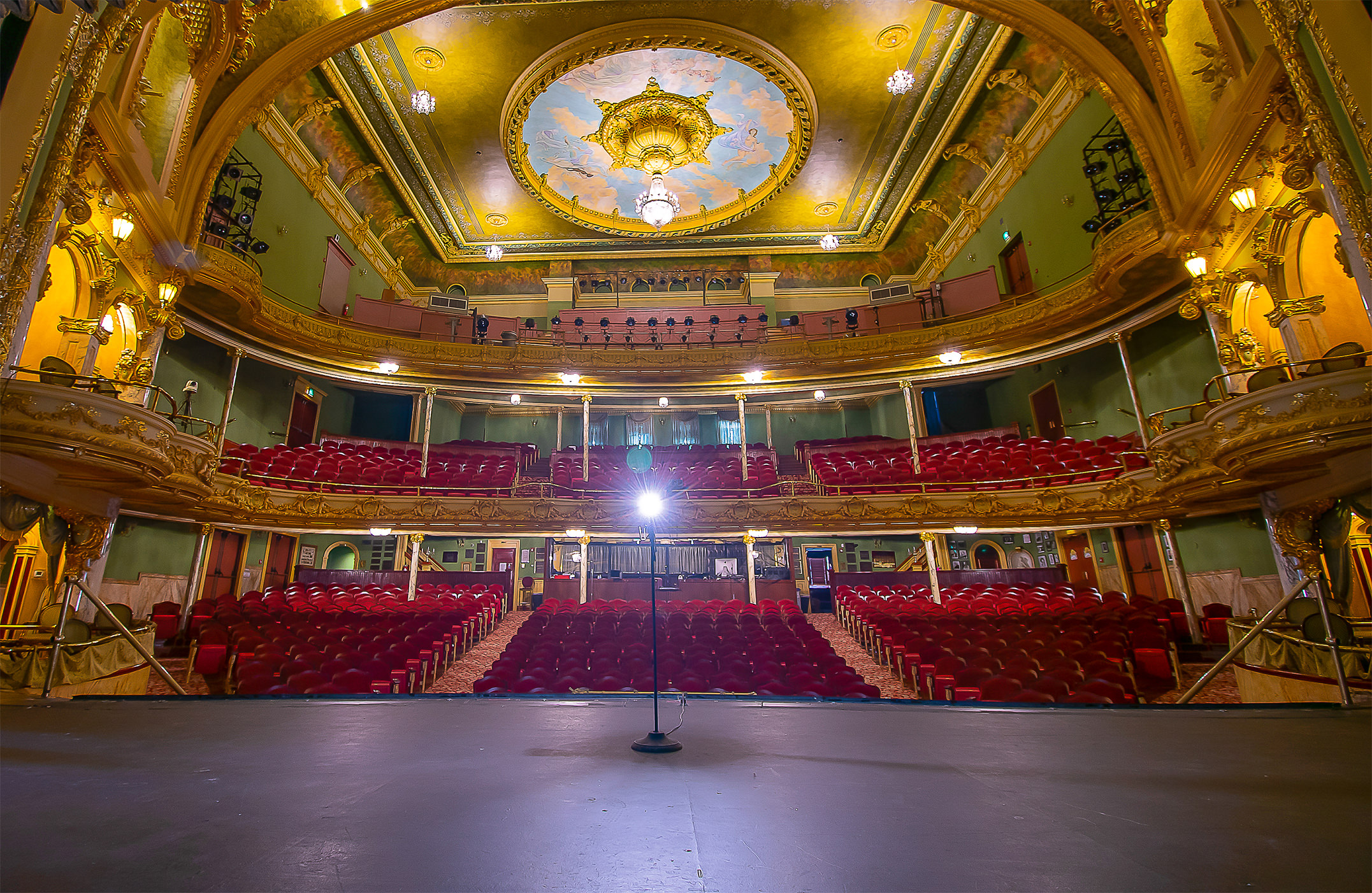 Theater interior with most seats filled, an orchestra in the pit, and the gray curtain is closed